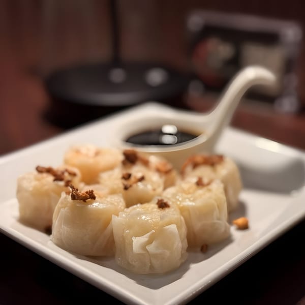 A plate of Thai O'Clock steamed dumplings with crispy garlic and a side of soy sauce.