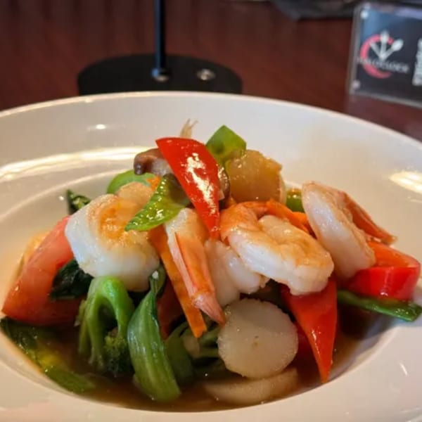 Thai O'Clock's stir-fried shrimp and scallops with colorful vegetables in a white bowl.
