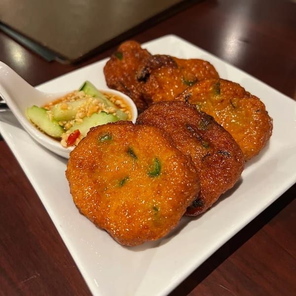 Five golden-brown Thai fish cakes with a side of cucumber relish on a white plate.