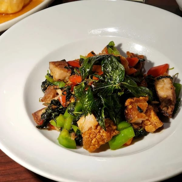 Crispy pork belly stir-fry with vibrant green basil, red peppers, and green vegetables on a white plate.