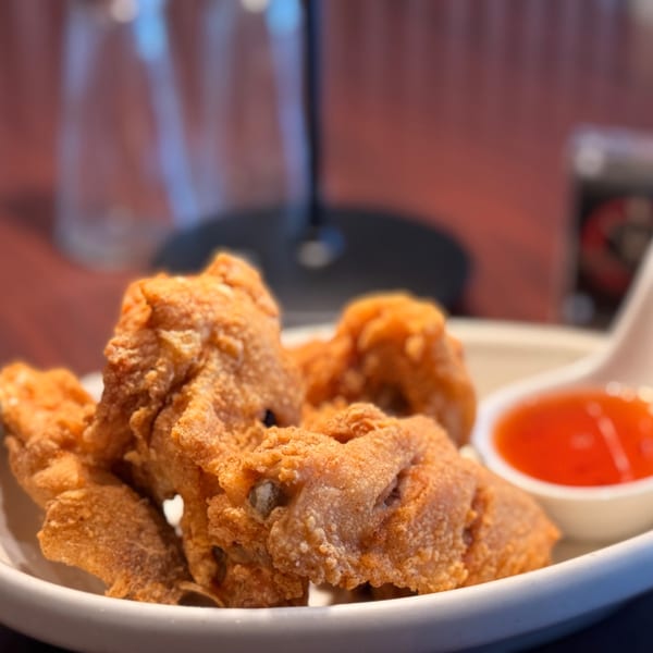 Crispy fried chicken pieces with a side of sweet chili sauce on a white plate at Thai O'Clock.