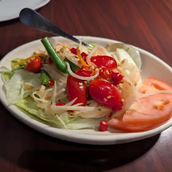 Spicy Thai papaya salad with cherry tomatoes, green beans, and shredded vegetables in a white bowl.