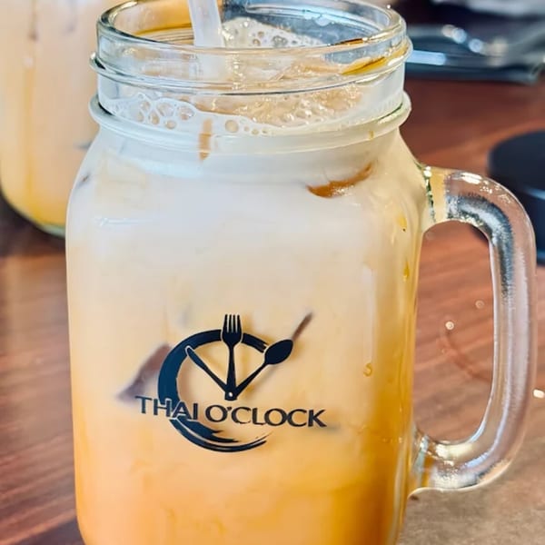 Iced Thai tea with a straw in a mason jar mug with the Thai O'Clock logo.